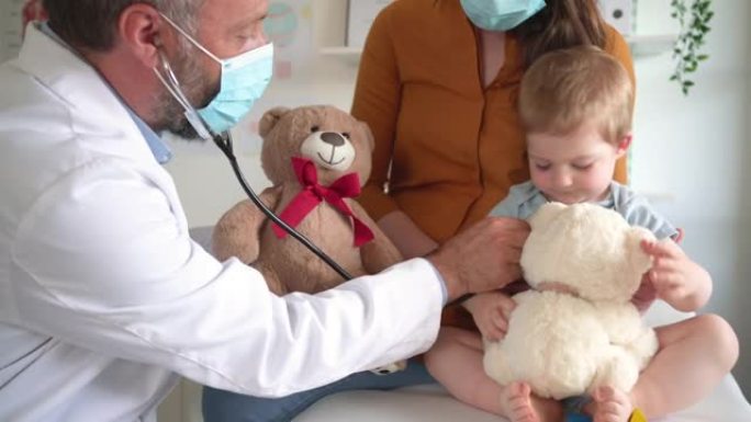 带有保护性面罩的儿科医生试图用听诊器检查哭泣的男婴