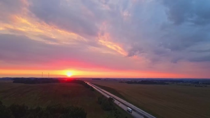 红色日落时高速公路的全景鸟瞰图。乡村田野附近有道路的景观。美丽的蜿蜒小路通向傍晚的乡村。戏剧性的天空