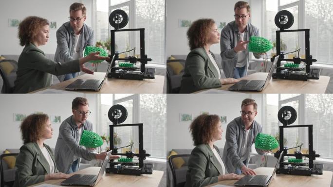 家用技术，现代男人和女人在客厅坐在桌子上的3D打印机上打印3D模型的原型
