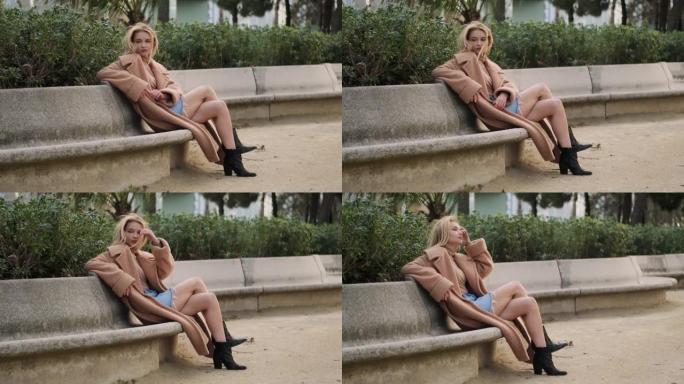 浪漫时尚的金发女孩梦dream以求地在城市公园的长凳上休息