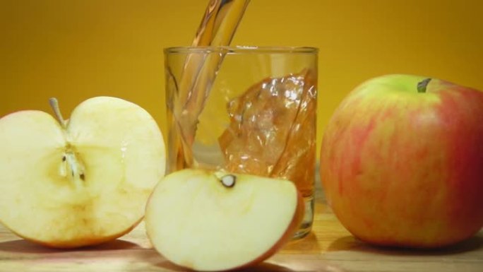 将苹果汁倒入黄色背景上苹果片旁边的玻璃杯中
