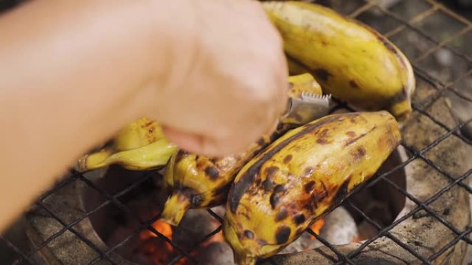 有人在传统的炭炉上翻转烤去皮的香蕉。烧烤食物。泰国菜。热带地区的甜果甜点。