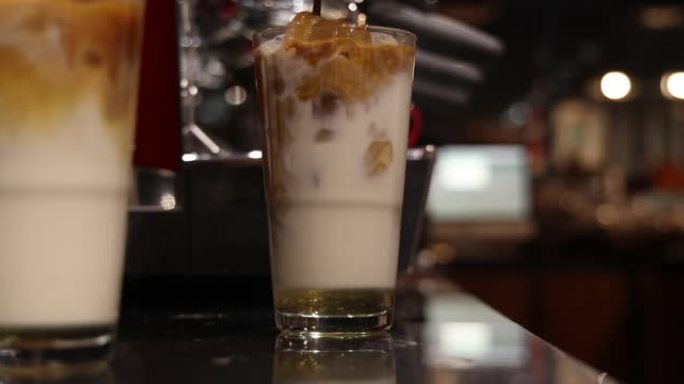 专业咖啡师在繁忙的咖啡店里将咖啡倒入加冰的玻璃杯中并添加牛奶