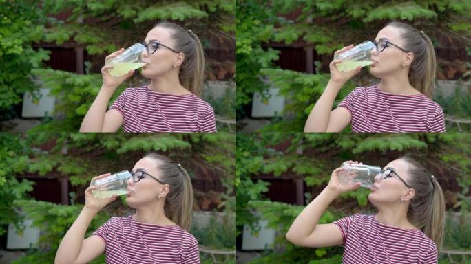 一个戴眼镜的女孩手里拿着一杯装有维生素饮料的杯子，一口喝。保持免疫力。健康的生活方式。