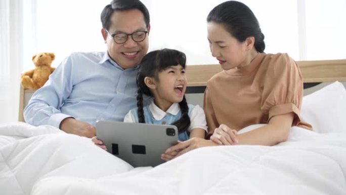 父母和他们的孩子在床上玩电子数字平板电脑