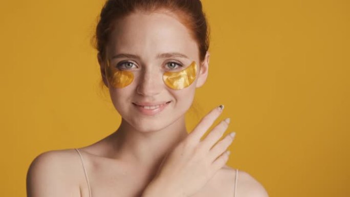 穿着金色眼罩的漂亮女孩在彩色背景上性感地在相机上摆姿势。美容概念