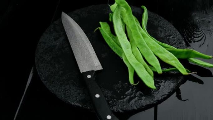 新鲜切好的青豆和一把刀放在质朴的黑色木桌上。