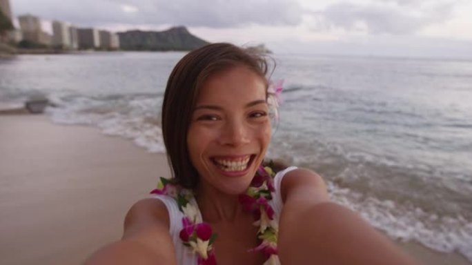 在威基基海滩自拍的亚洲女人。微笑美丽的女游客在度假时穿着兰花蕾花环。檀香山的女孩在镜头前皱着嘴唇吹吻