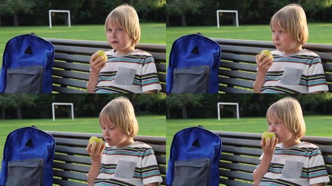 面带微笑的小学生小孩背着背包坐在校园的长凳上，放学后或课间休息时吃零食。