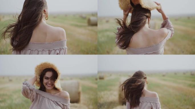 女孩走在多风的麦秸田间，转身对着镜头，戴上帽子微笑