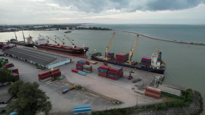 无人机拍摄了一艘坐在港口码头上的货船，起重机吊杆下降到适当的位置以卸下集装箱。