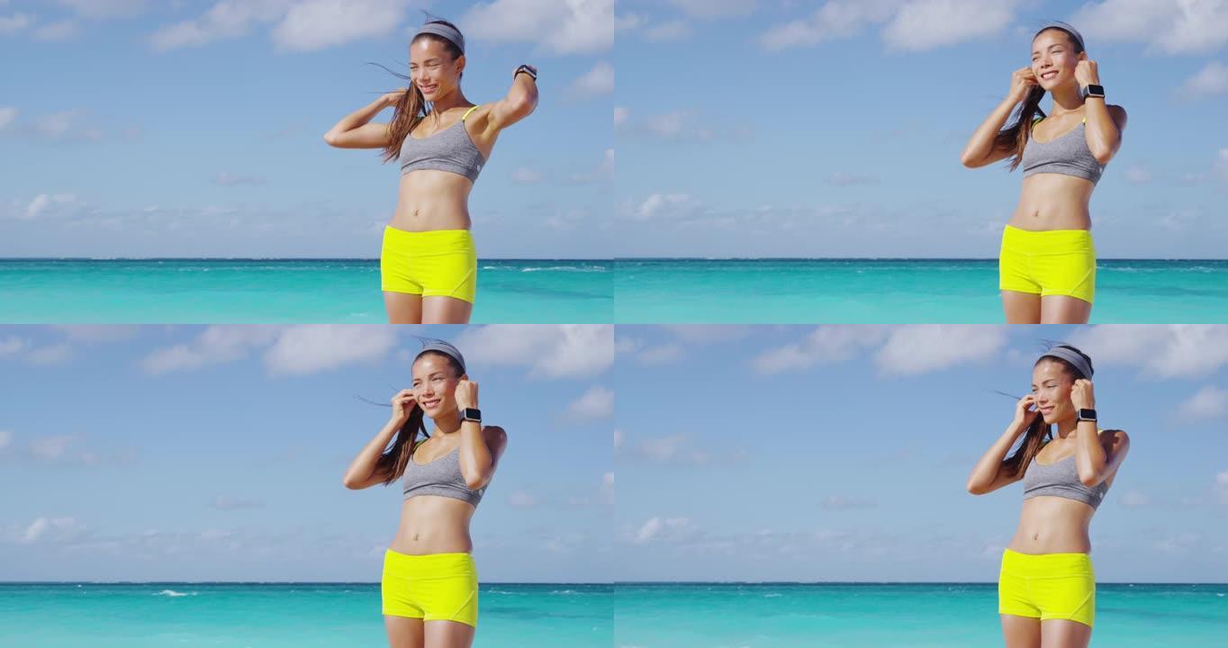 跑步女孩戴着耳机和跑步臂章电话臂带准备跑步锻炼。在阳光明媚的海滩暑假锻炼时戴上耳机听音乐的手势。