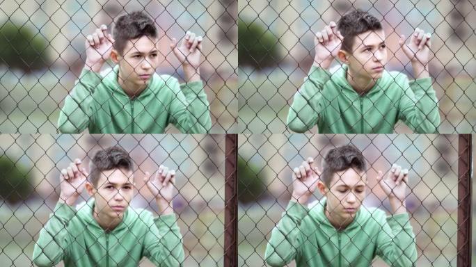 难民悲伤的男孩独自一人低头在篱笆附近，垂下眼睛，拍摄电影