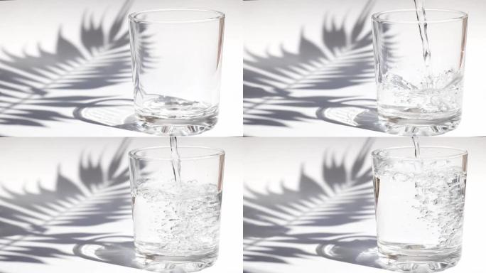清澈的水倒入桌上的酒杯中，并带有棕榈叶阴影。排毒和夏季茶点饮料概念。特写