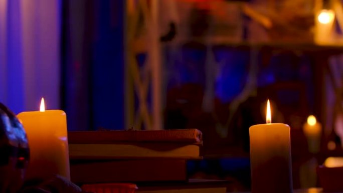 一个有着可怕面孔的南瓜躺在黑暗的房间里，在书本上，在燃烧的蜡烛旁边。女孩的手移开南瓜，然后将其放回原