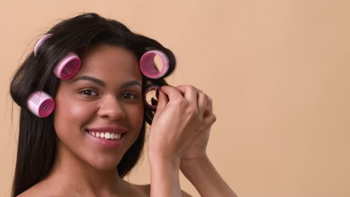 非裔美国妇女卷发应用卷发器在米色背景