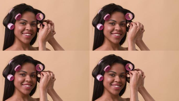非裔美国妇女卷发应用卷发器在米色背景