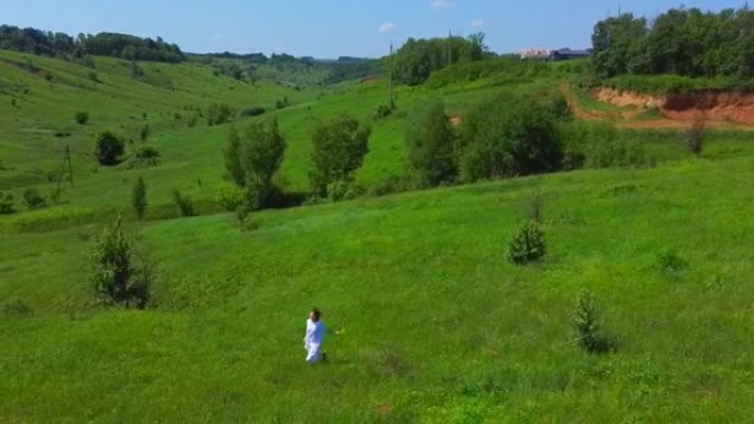 一个女人在绿野的航拍。一个年轻女孩在山上散步和采花。无人机飞越人与自然。夏天快乐。享受这一刻。