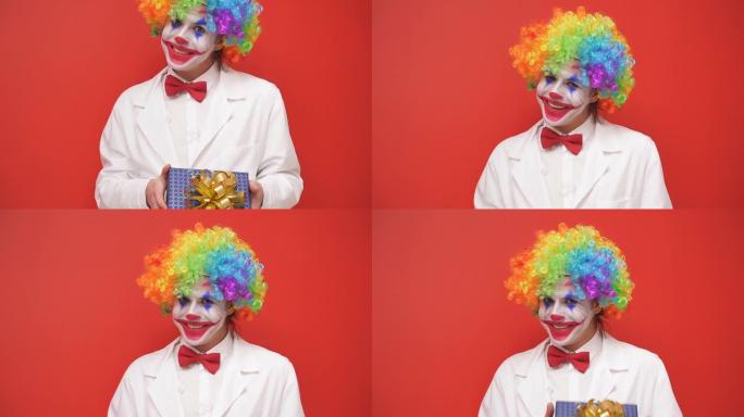 一个快乐的小丑在镜头前摆姿势，在孤立的背景上有一个礼品盒