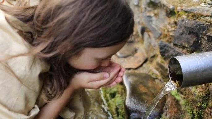 小女孩在大自然中喝干净的泉水。山区饮用水来源。