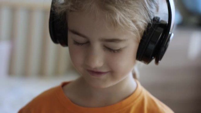 戴着耳机听音乐的可爱小女孩的肖像。孩子戴着耳机闭着眼睛放松时的慢动作。孩子在家听音乐。快乐无忧无虑的