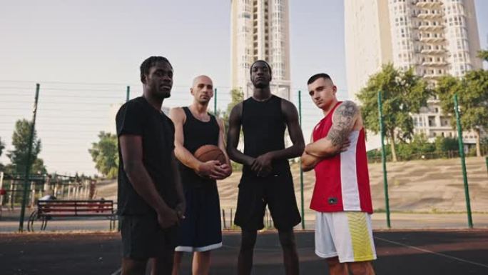 篮球队。缩小篮球场上多民族运动员团队的肖像。穿着运动服和篮球的高加索人和非洲人朋友