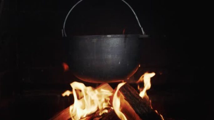 一桶沸腾的肉汤的铸铁桶挂在明火上的燃木火炉中。慢动作视频