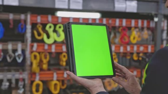 4k视频片段，一个无法识别的女人在仓库中拿着带有绿色屏幕的数字平板电脑