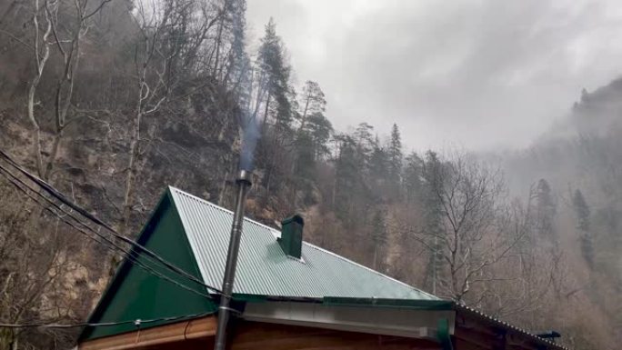 在山区用烟囱封闭建筑屋顶。烟雾从烟囱滚滚到周围的大气中