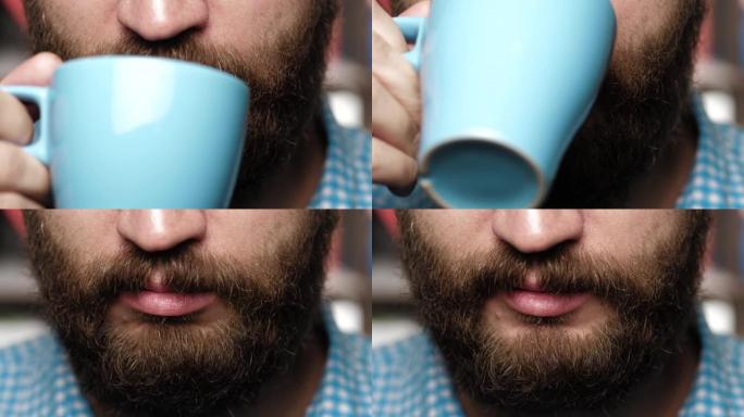 大胡子的人正在喝咖啡或茶。男性的手将蓝色的杯子带到她的嘴里，并从中喝咖啡或茶。特写