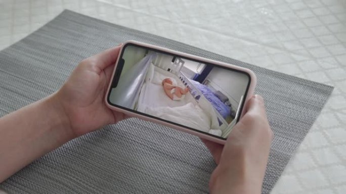 母亲使用ip无线安全摄像头作为手机上的婴儿视频监视器，女人实时看着她熟睡的婴儿