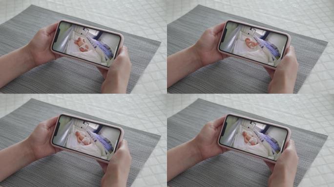 母亲使用ip无线安全摄像头作为手机上的婴儿视频监视器，女人实时看着她熟睡的婴儿