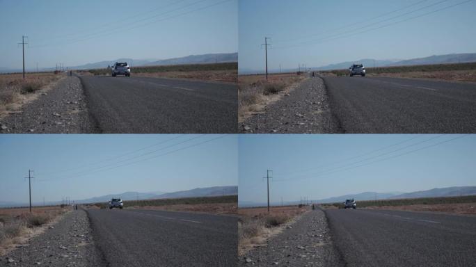 汽车开走的低角度视图。在乡村干燥多尘的景观中，穿过道路的电线。摩洛哥、非洲