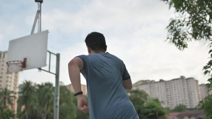 慢动作后视亚洲中国中年男子在周末阴天早上在篮球场跑步