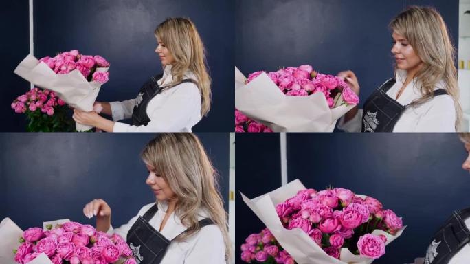 女性花店手里拿着美丽的粉红玫瑰花束，享受工作成果。花店助理为约会或生日派对订单收集玫瑰安排