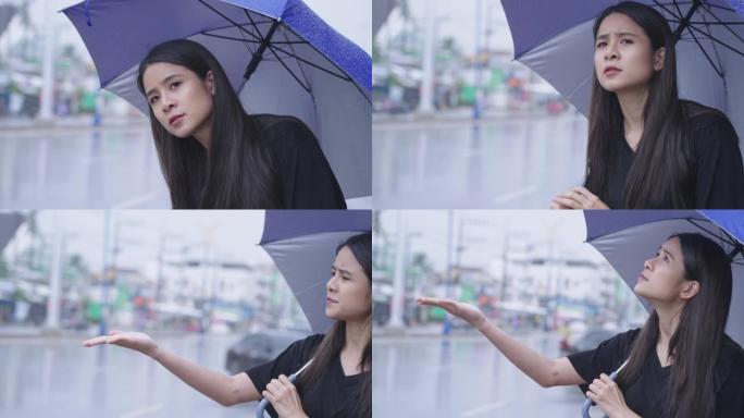 一个美丽的东亚妇女独自站在路边等待出租车或公共汽车，在下雨的时候，在雨中撑伞，在高峰时间，热带气候变