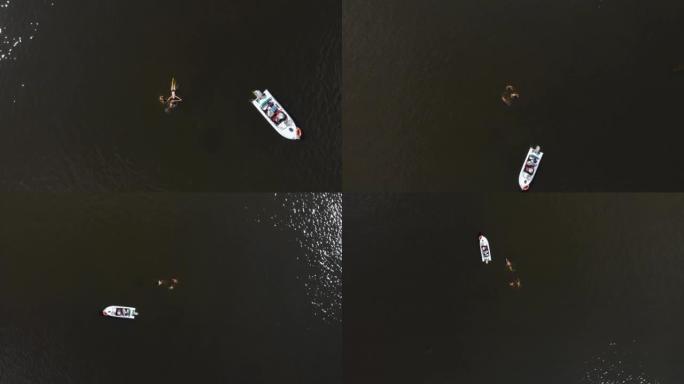 三个朋友游泳，夏天在一个大水湖上划船。白色摩托艇停泊在附近，水在阳光下闪烁。顶角航空无人机螺旋全景