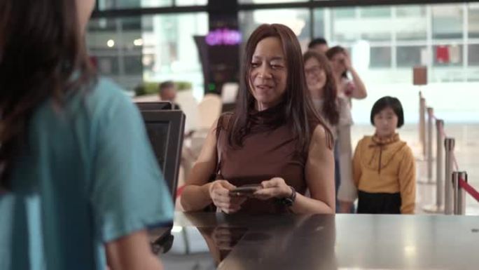 亚洲华人女性客户在售票柜台使用非接触式支付移动应用程序购买机票。