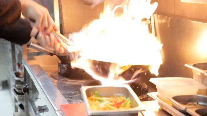 厨师的手将水包倒在热油中的锅中，在燃气灶火焰上
