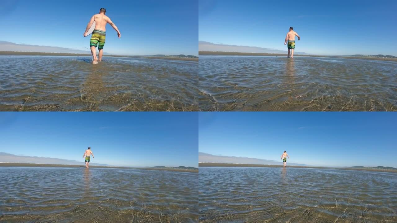 男子手持脱脂板在沙滩潮汐池中慢动作行走
