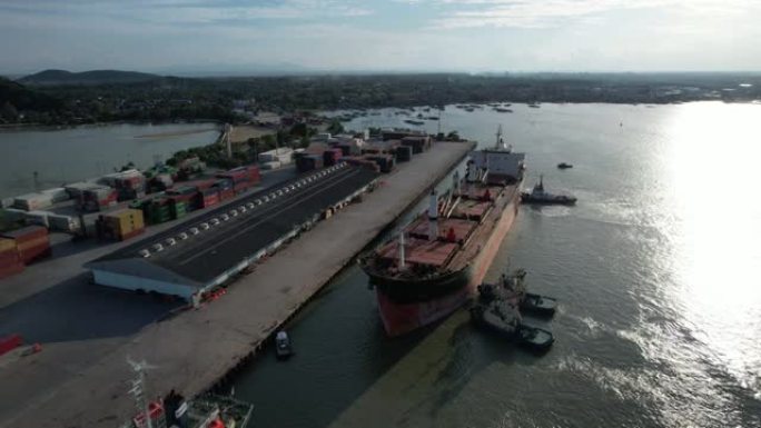 无人机拍摄了一艘坐在港口码头上的货船，起重机吊杆下降到适当的位置以卸下集装箱。