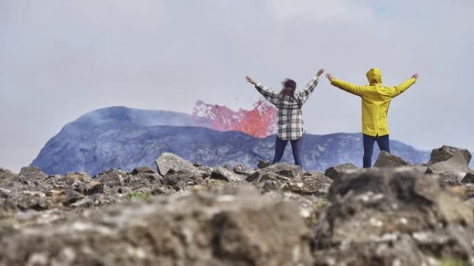 当两名大胆的游客高举双手时，无人驾驶飞机拍摄了一座喷发的火山