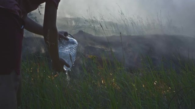 志愿者男子或男孩扑灭野火。从塑料瓶里倒水。雨林野火灾害，干灌木丛燃烧，火灾原因。