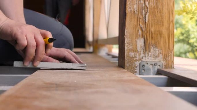修回家。地板安装露台。木匠在木板上画了一条切割线。用角尺关闭测量地板。用铅笔和仪表标记在木板上测量的