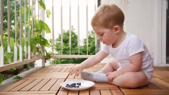 可爱的男婴坐在家里的阳台上吃蓝莓
