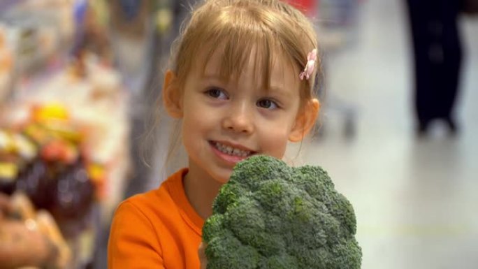 购物车里的小女孩在超市的蔬菜部门选择西兰花。健康素食。商店里的儿童购物食品。