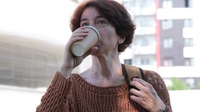 成熟的女人在城市街道上等待，并从纸杯中喝咖啡