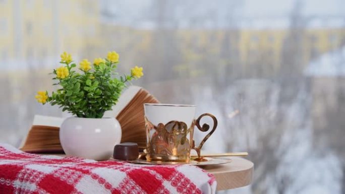 咖啡馆里的金色咖啡杯、书和带鲜花的花瓶。冬天，外面下雪。舒适的氛围