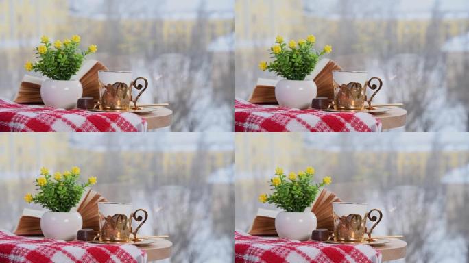 咖啡馆里的金色咖啡杯、书和带鲜花的花瓶。冬天，外面下雪。舒适的氛围