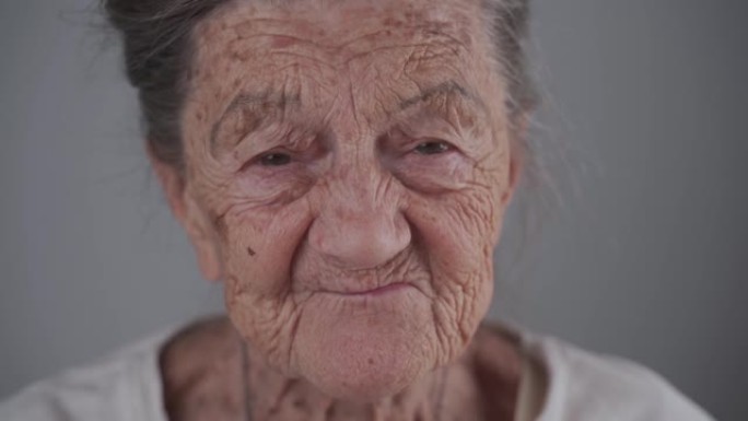 90岁的高加索无牙高级女性肖像，有着深深的皱纹和白发可爱的微笑和在工作室的灰色背景上交谈。有牙齿问题